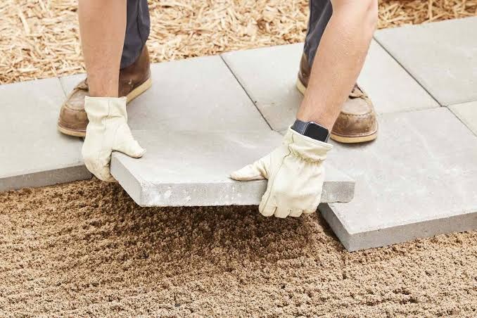 Gloved hands setting a large paver on a leveled sand base