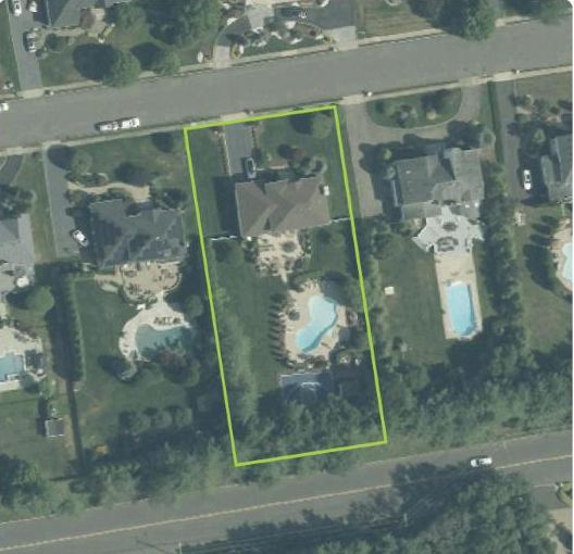Aerial photo of a suburban street with one lot outlined in green, showing the house, a pool and the lawn around it